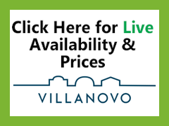 A white sign with black and green text reads, Click Here for Live Availability & Prices. Below is a blue outline of buildings and the word VILLANOVO, highlighting premium Villas and Chalets. The sign is framed by a green border.